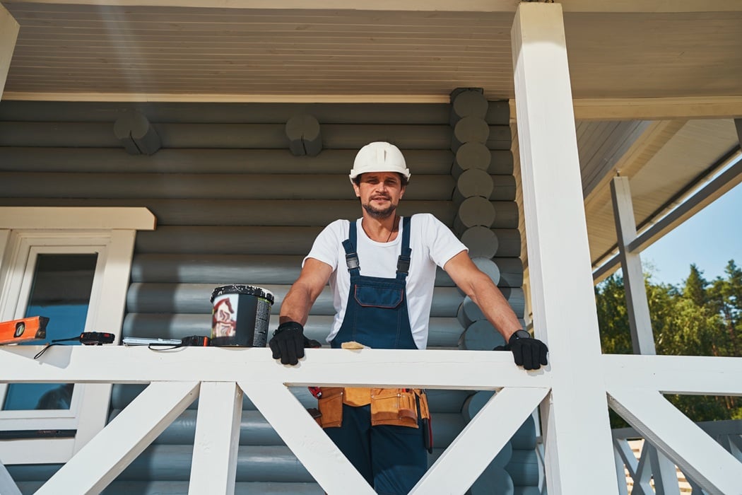 Worker in a hard hat and tool belt behind the white railing of a deck under construction